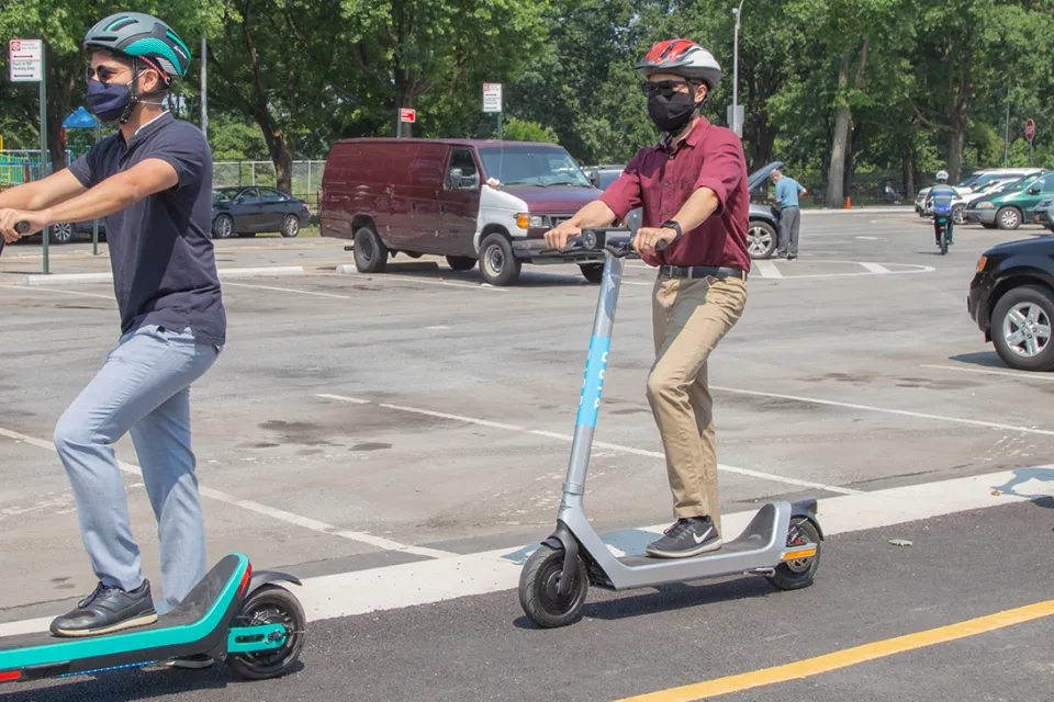 Three people wearing helmets riding electric scooters in New York City